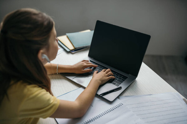 blurred girl studying at home and typing on laptop near copybooks and papers