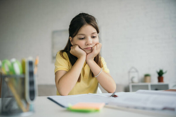 bored and thoughtful girl sitting with hands near face during homeschooling