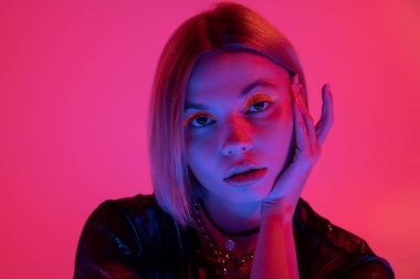 Neon makyajlı güzel bir kadının portresi. Mavi ışıkta, derin pembe arka planda el ele tutuşmuş.