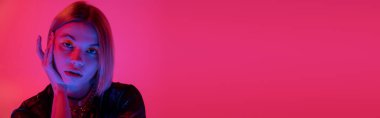 Parlak neon ışıklı genç bir kadının portresi. Pembe arka plandaki kameraya bakıyor.