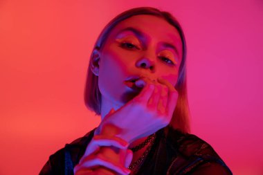 Neon yüzlü şık bir kadın. Yüzü mercanlara yakın ve pembe arka planda poz veriyor.