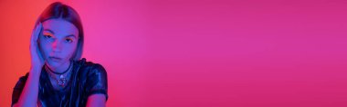 Mercan ve pembe arka planda mavi neon ışıkla parlak neon makyajlı genç bir kadının portresi.
