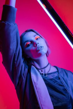 Neon makyajlı, kolyeli, floresan lambalı, koyu pembe ve mercan arka planlı moda bir kadın.