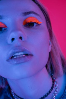Parlak neon farlı bir kadının portresi. Derin pembe arka planda mavi ışıkta kameraya bakıyor.