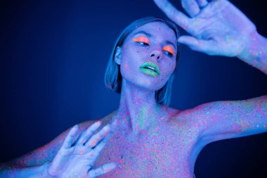 nude and sensual woman with neon makeup and colored body posing on dark blue background clipart
