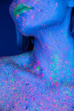 Koyu mavi üzerine izole edilmiş neon renkli vücut boyası giymiş genç bir kadının kısmi görüntüsü