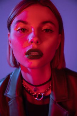 Parlak makyajlı bir kadının portresi mor üzerine izole edilmiş kırmızı ışıkta kameraya bakıyor.