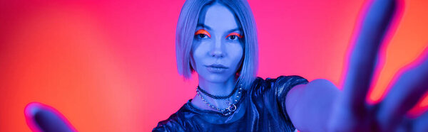 woman in necklaces posing with outstretched hands in blue neon light on coral and pink background, banner
