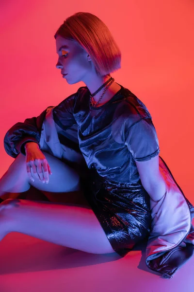 Modaya uygun bir kadının mavi ışıkta mercan kırmızısı arka planda oturması.