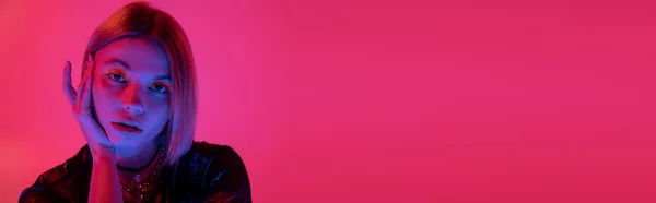 stock image portrait of young woman in bright neon light looking at camera on deep pink background, banner