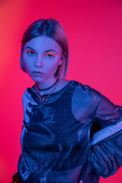 pretty woman in neon makeup looking at camera in blue light on pink and coral background