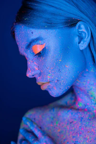 profile of woman with vibrant makeup posing in neon light isolated on dark blue