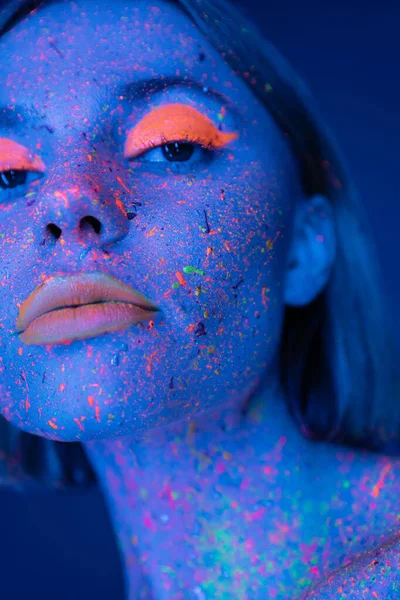 stock image close up portrait of woman in glowing neon makeup and bright paint isolated on dark blue
