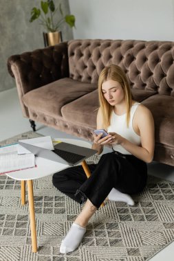 Genç koç dizüstü bilgisayarın yanında akıllı telefon ve evde not defteri kullanıyor. 