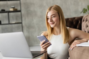 Pozitif koç evde çalışırken bilgisayarın yanında akıllı telefon tutuyor. 