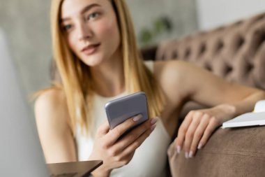 Bulanık koç dizüstü bilgisayar ve defterin yanında akıllı telefonu evdeki kanepede tutuyor. 