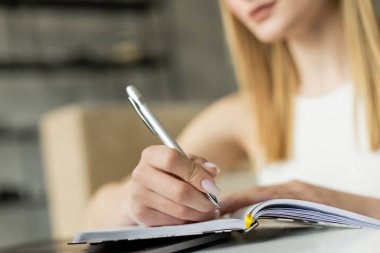 Cropped view of blurred woman writing on notebook near laptop during online education at home  clipart