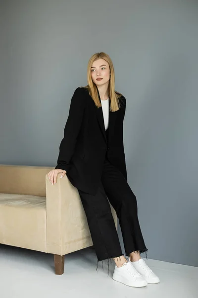 stock image Full length of pretty blonde woman in jacket standing near couch at home 