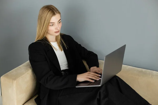 stock image Pretty blonde coach looking at laptop while sitting on beige sofa 