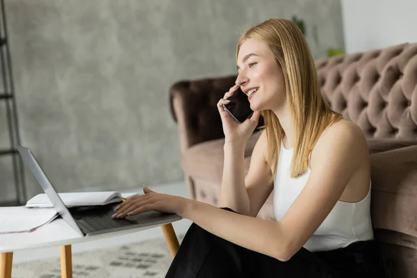 stock image Positive blonde coach talking on smartphone and using laptop at home 