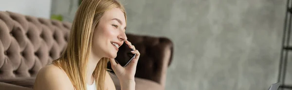 stock image Positive blonde coach talking on cellphone near blurred laptop at home, banner 