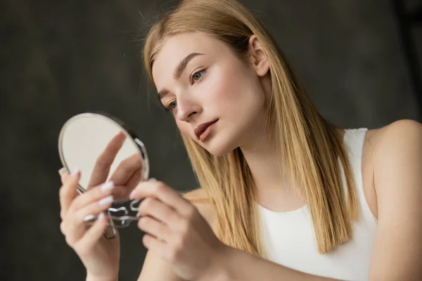 stock image Pretty blonde woman in white top holding mirror at home in morning  