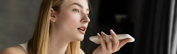 Stock image Blonde woman recording audio message on smartphone at home, banner 