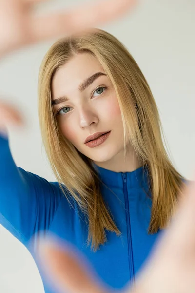 stock image blonde and pretty woman with blurred outstretched hands looking at camera isolated on grey