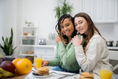 Neşeli lezbiyen kadın kahvaltıda gülümseyen Afrikalı Amerikalı kız arkadaşına sarılıyor. 