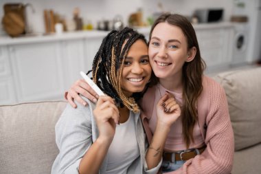 happy african american and lesbian woman holding pregnancy test near smiling girlfriend  clipart