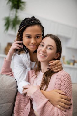 Mutlu Afro-Amerikan lezbiyen kadın oturma odasında neşeli kız arkadaşına sarılıyor. 