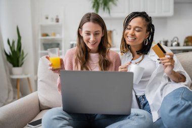 Genç Afrikalı Amerikalı lezbiyen kız arkadaşının yanında internetten alışveriş yaparken dizüstü bilgisayar kullanıyor. 