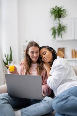 Dövmeli Afro-Amerikan lezbiyen kadın mutlu kız arkadaşına yaslanıyor evde çalışırken laptop kullanıyor. 