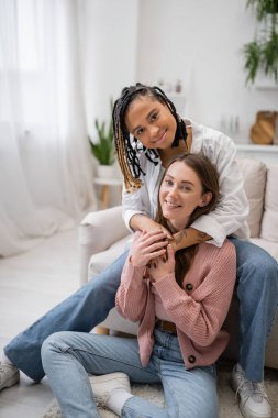 Neşeli Afro-Amerikan lezbiyen kadın Rastalı sarılan kız arkadaşı oturma odasında 