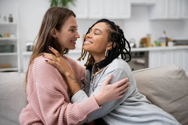 happy and tattooed african american lesbian woman with engagement ring hugging smiling girlfriend