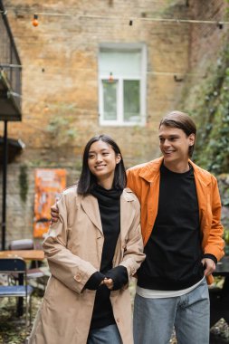 Gülümseyen adam açık kafede Asyalı kız arkadaşına sarılıyor. 