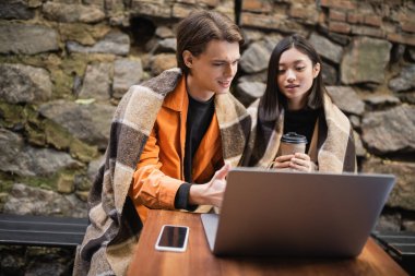 Kahve içen ırklar arası bir çift kafenin terasında dizüstü bilgisayar kullanıyor. 