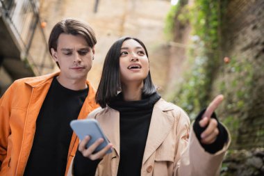 Asyalı genç bir kadının akıllı telefon kullanması ve açık havada erkek arkadaşının yanında işaret etmesi düşük açı. 