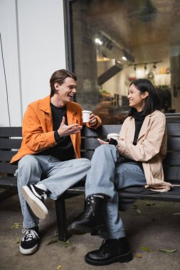 Kafenin yanındaki bankta oturan Asyalı bir adamla kağıt bardakla konuşan olumlu bir adam. 