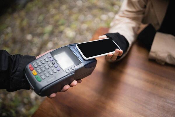 Cropped view of woman paying with cellphone in outdoor cafe 