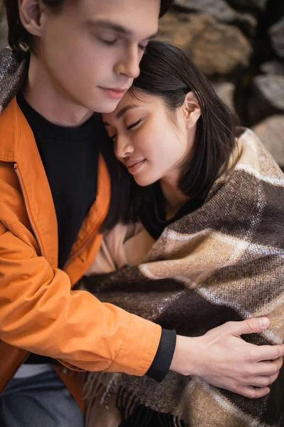 stock image Young man hugging asian girlfriend covered in blanket in outdoor cafe 