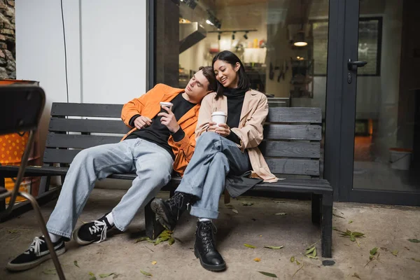 Kahve tutan şık bir adam, kafenin terasındaki bankta oturan neşeli Asyalı kız arkadaşının yanına gitmek için. 