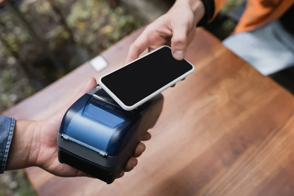 stock image Cropped view of man paying with smartphone near waitress with payment terminal in cafe 