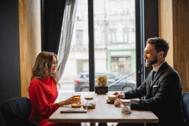 side view of happy couple looking at each other near drinks on table  clipart