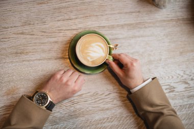 top view of cropped man holding cup of cappuccino with latte art  clipart