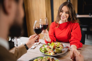 Kırmızı şarap kadehlerini tokuştururken erkek arkadaşıyla el ele tutuşan neşeli bir kadın. 