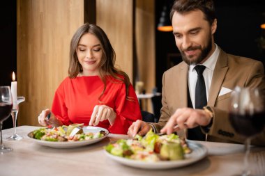 happy young couple in festive attire looking at tasty salad during celebration on valentines day  clipart