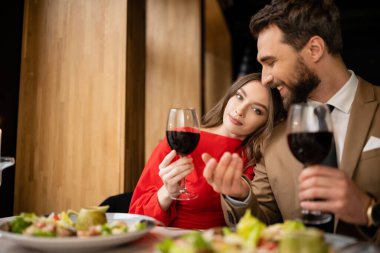 Sevgililer Günü 'nde kutlama sırasında elinde kırmızı şarapla kadeh tutan genç bir kadın ve neşeli bir adam. 