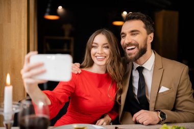 Sevgililer Günü 'nde kutlama sırasında bir erkekle selfie çekerken elinde akıllı telefon tutan neşeli kadın. 