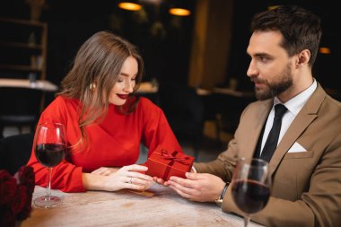 bearded man holding wrapped present near happy young woman on valentines day  clipart